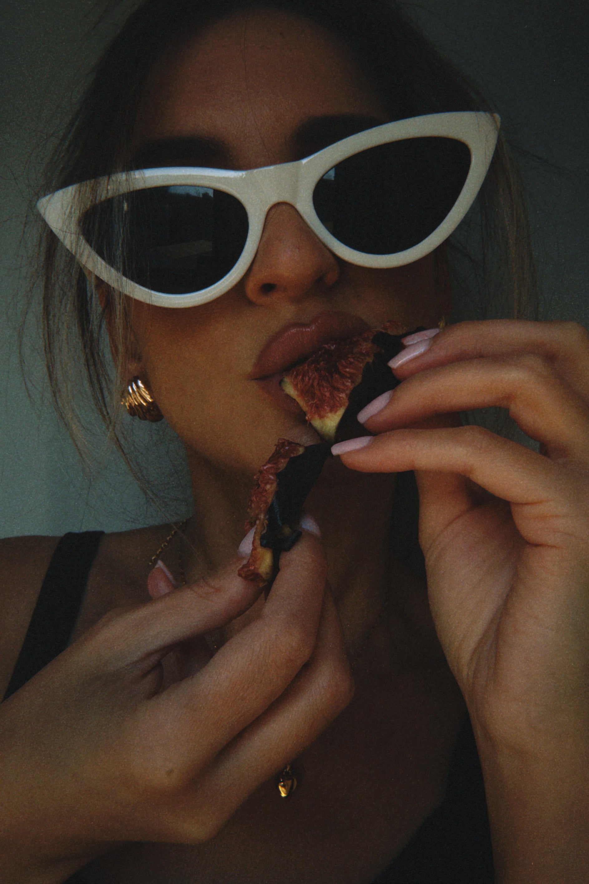 Person wearing white sunglasses eating a fig.