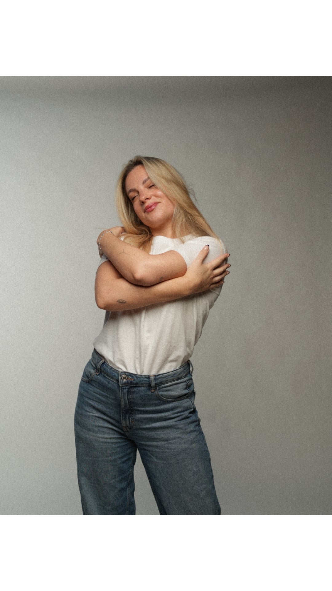 Woman wearing a white shirt from the wildest fig and blue jeans against a gray background