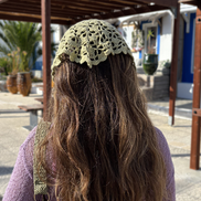 Person wearing a sage green knitted headscarf in an outdoor setting with buildings and plants. for the wildest fig crochet collection