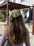 Person wearing a sage green knitted headscarf in an outdoor setting with buildings and plants. for the wildest fig crochet collection