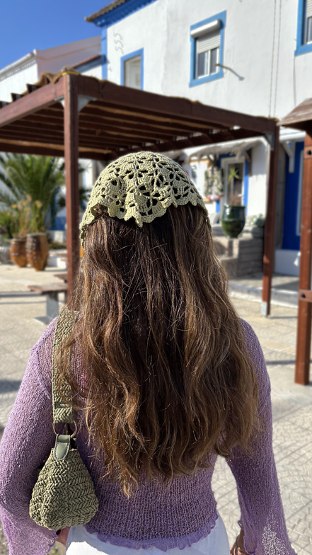 Person wearing a sage green knitted headscarf in an outdoor setting with buildings and plants. for the wildest fig crochet collection